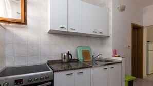 Une cuisine avec des armoires blanches, une cuisinière en acier inoxydable, une planche à découper verte et un évier.