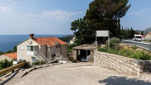 Un bâtiment situé sur la côte, avec un toit recouvert de tuiles rouges, un escalier menant à un balcon et une vue sur la mer.