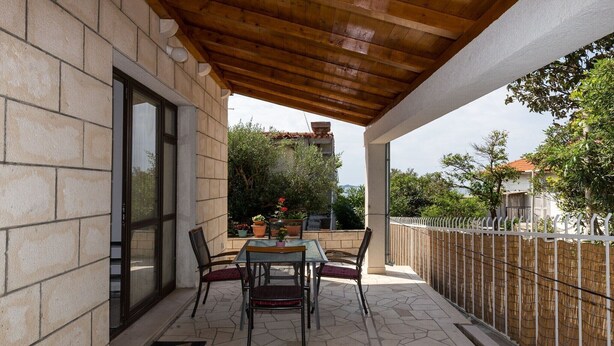 Une terrasse extérieure avec une table et des chaises, une pergola en bois, des murs en pierre et une vue sur un quartier résidentiel.