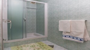 Une douche avec une porte en verre, un porte-serviettes avec plusieurs serviettes et un tapis à motifs sur le sol.