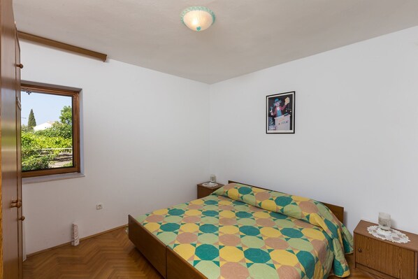 A bedroom with a bed, a nightstand, a window, and a framed picture on the wall.