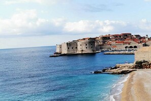 A coastal cityscape with historic architecture, including a prominent fortress-like structure and a beach. - Apartments Pojko - One-Bedroom Apartment with Terrace (Yellow) (Dubrovnik)