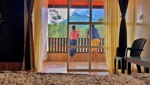 A room with a view of a mountain through a glass door. There is a chair and a table inside the room. - Nature Kingdom (Chikkamagaluru)