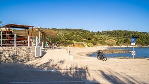 A coastal road with a stone wall, a covered area, and a beach. - Apartments Nikolina (LU) - Studio with Sea View (3 Adults) (Lumbarda)