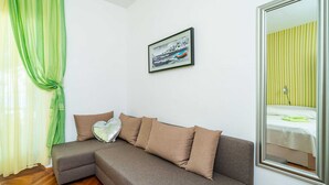 Una habitación moderna con un sofá seccional gris, un cuadro enmarcado de un barco y un espejo que refleja una cama con cortinas a rayas.