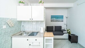 A compact kitchen with a sink, cabinets, and a small table. There is a sofa and a painting in the adjacent living area.