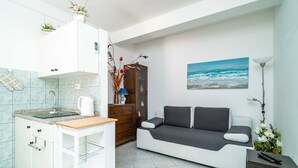 A compact living space with a kitchenette, a sofa, and a painting of the ocean.