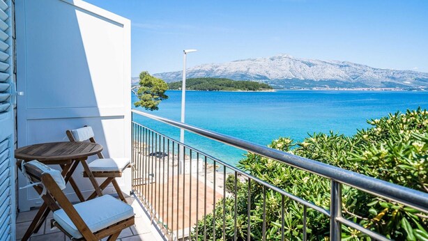 A balcony with a view of a clear blue sea and snow-capped mountains.