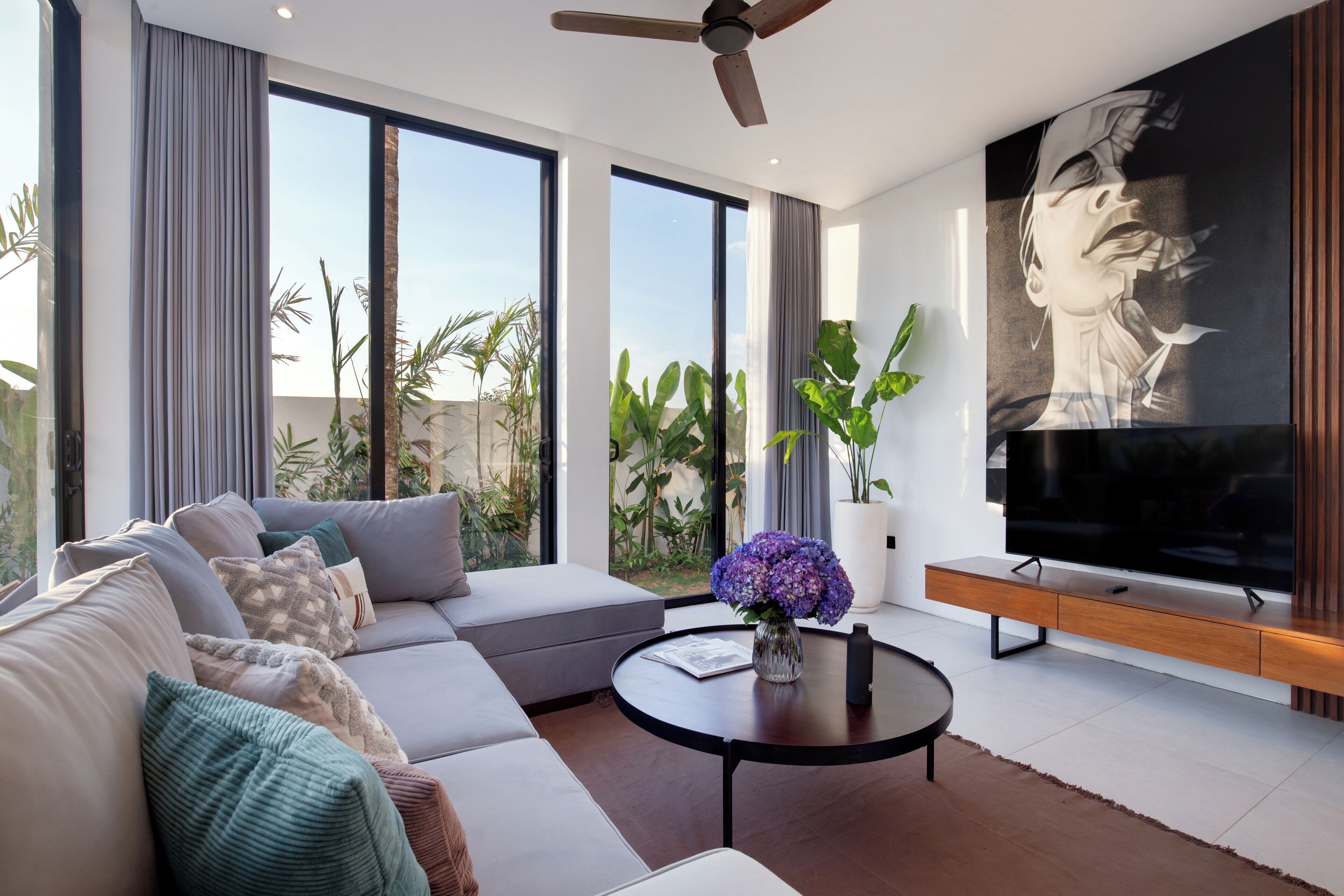 A modern living room with a large window, a ceiling fan, a sofa, a coffee table, and a TV.