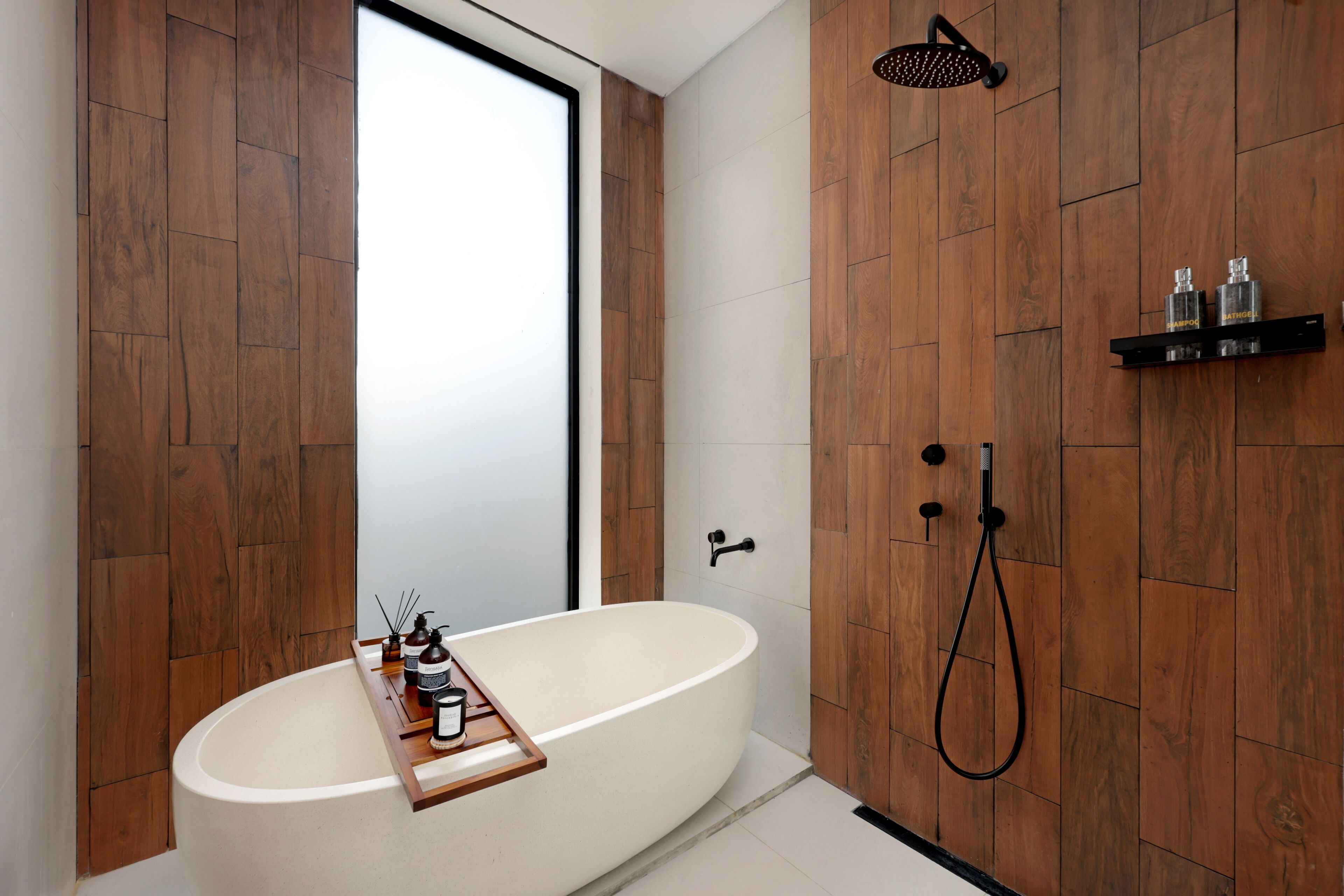 A modern bathroom with a freestanding bathtub, a showerhead, and a shelf with toiletries.