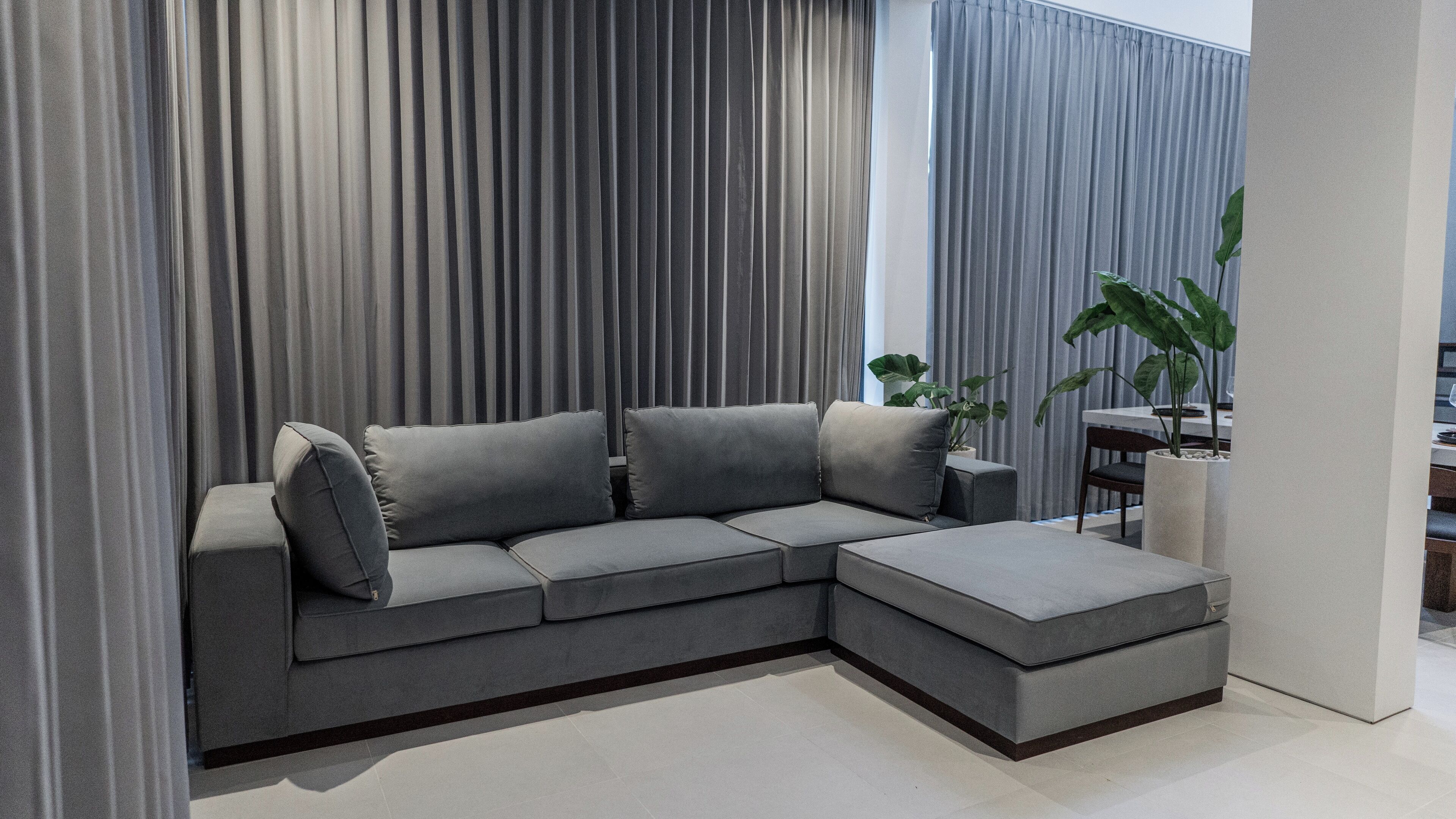 Un salon moderne avec un canapé d’angle gris, une petite table et une plante en pot.