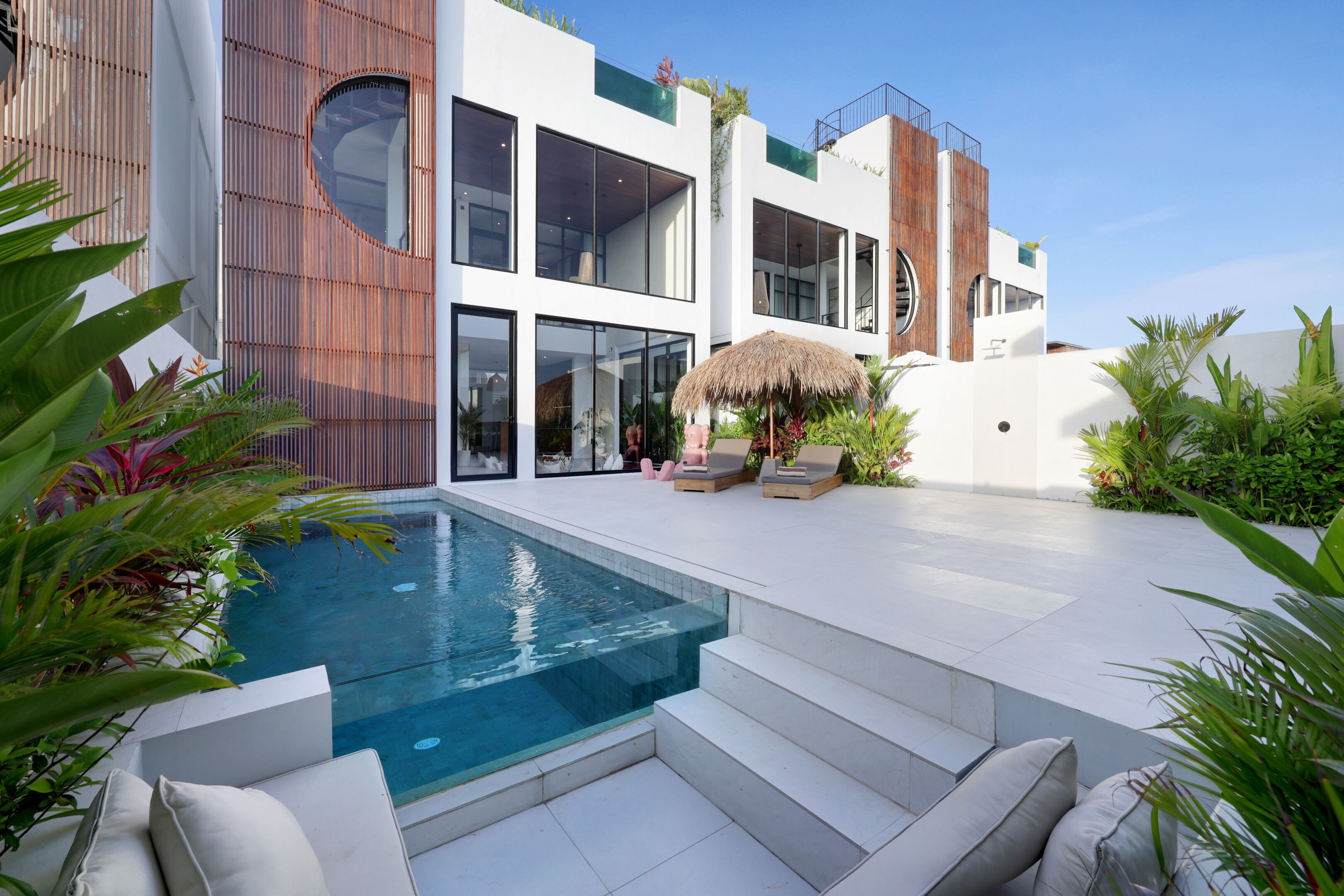 A modern house with a swimming pool, outdoor seating, and lush greenery.
