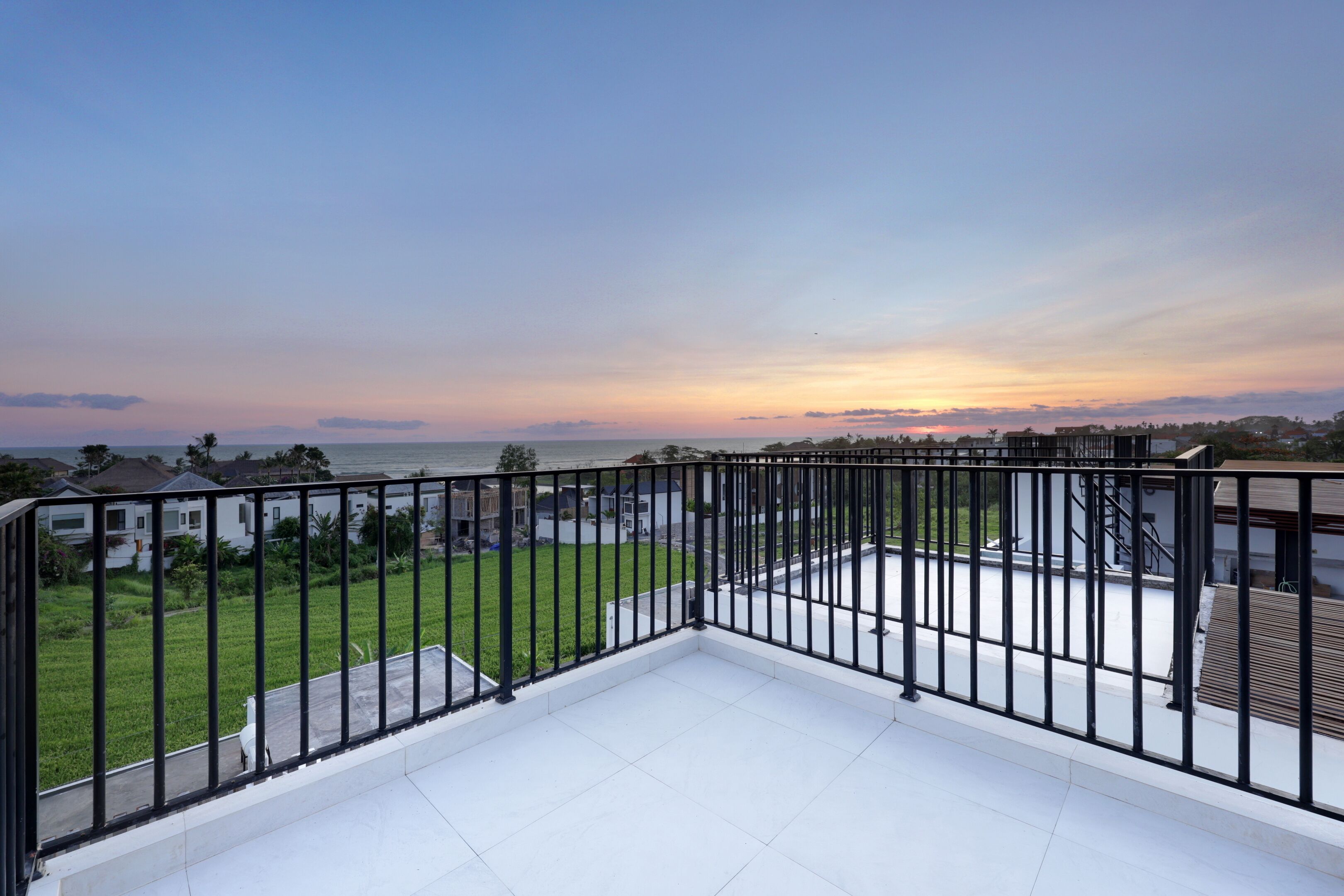 A balcony with a view of a residential area and a body of water during sunset.