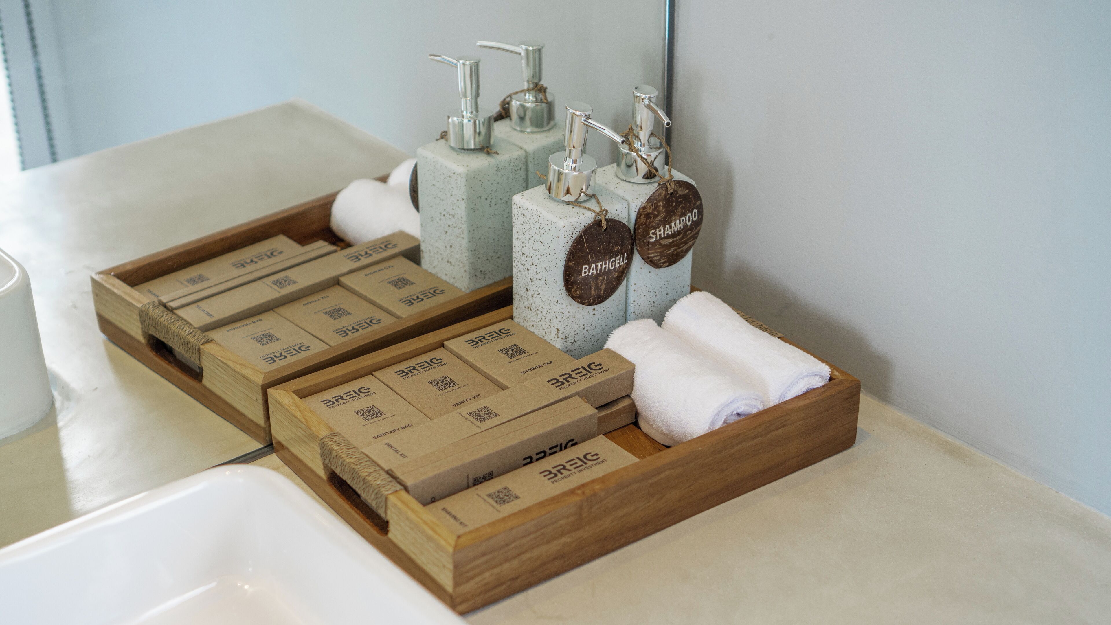 A bathroom with wooden boxes labeled 'BREIC' containing various toiletries, a shower cap, and a towel.