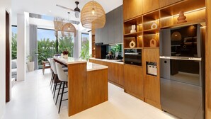 A modern kitchen with wooden cabinetry, a central island, and a built-in refrigerator. - Aquamarine Villas III (Munggu)