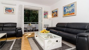 Una sala de estar moderna con un sofá de cuero negro, una mesa de centro de vidrio con fruta y obras de arte en las paredes.