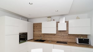 Una cocina moderna con armarios blancos, salpicadero de madera, horno empotrado, un lavabo y un microondas.
