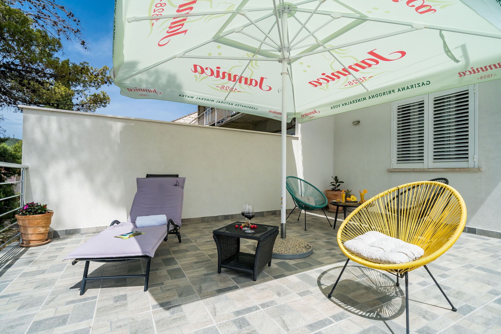 A patio with a lounge chair, a yellow chair, and an umbrella.