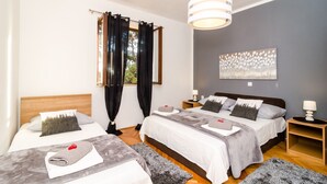 A hotel room with two beds, a grey wall, a ceiling light, and a window with curtains.