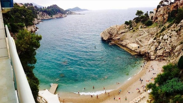 A coastal beach with rocky cliffs and clear blue water.