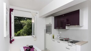 A compact kitchen with white cabinets, a built-in oven, and a window with a view of greenery. - Apartments Posta - One-Bedroom Apartment with Terrace and Sea View - Apartman 5 (Saplunara)