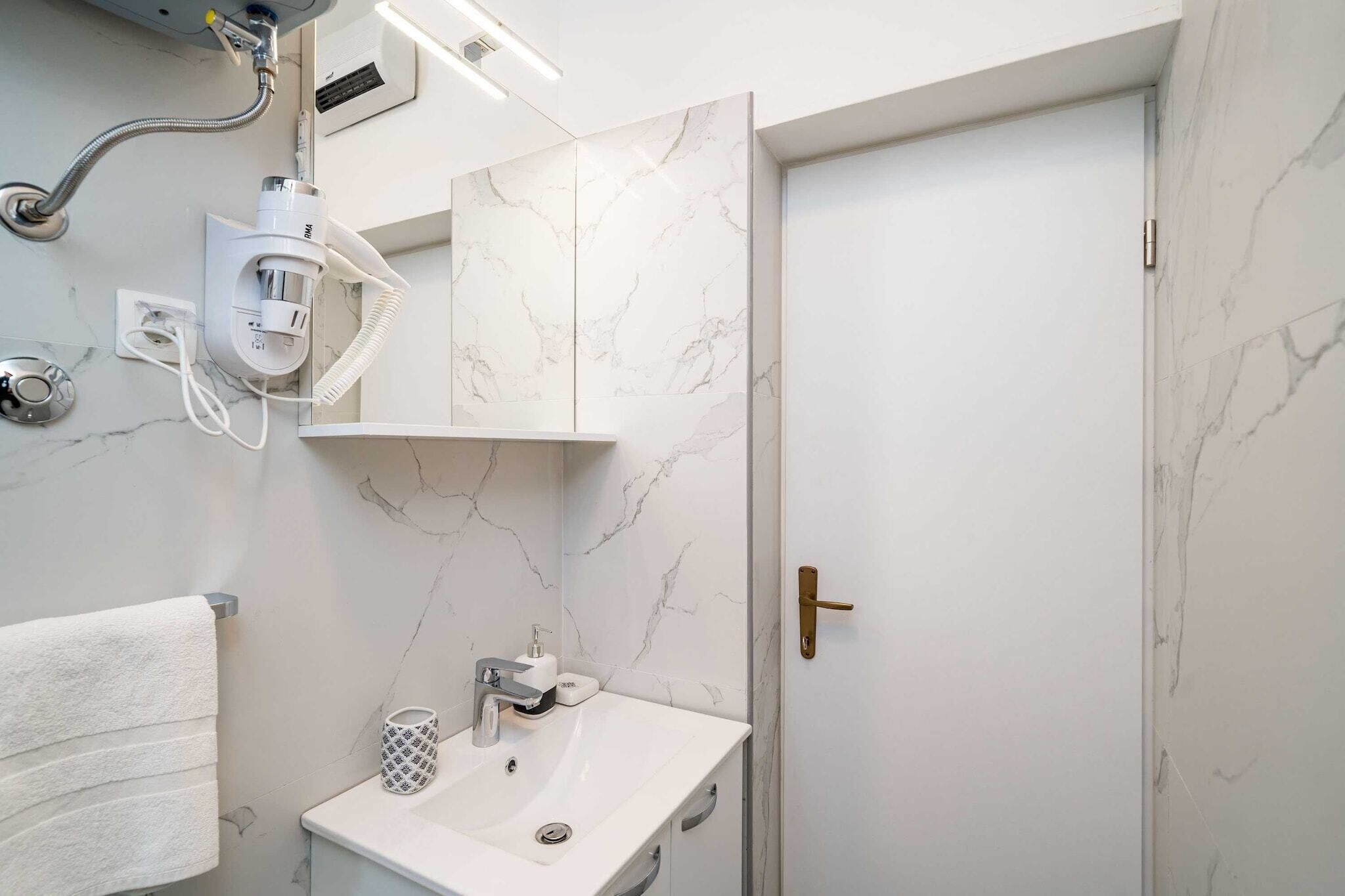 Un baño moderno con pared de mármol blanco, lavamanos integrado, perchero y ducha.