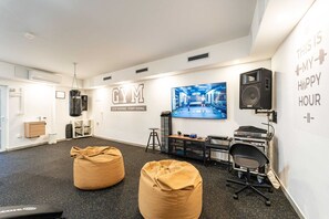 A modern gym with black and white walls, a large mirror, and a motivational quote. There are two bean bags, a treadmill, and a speaker.