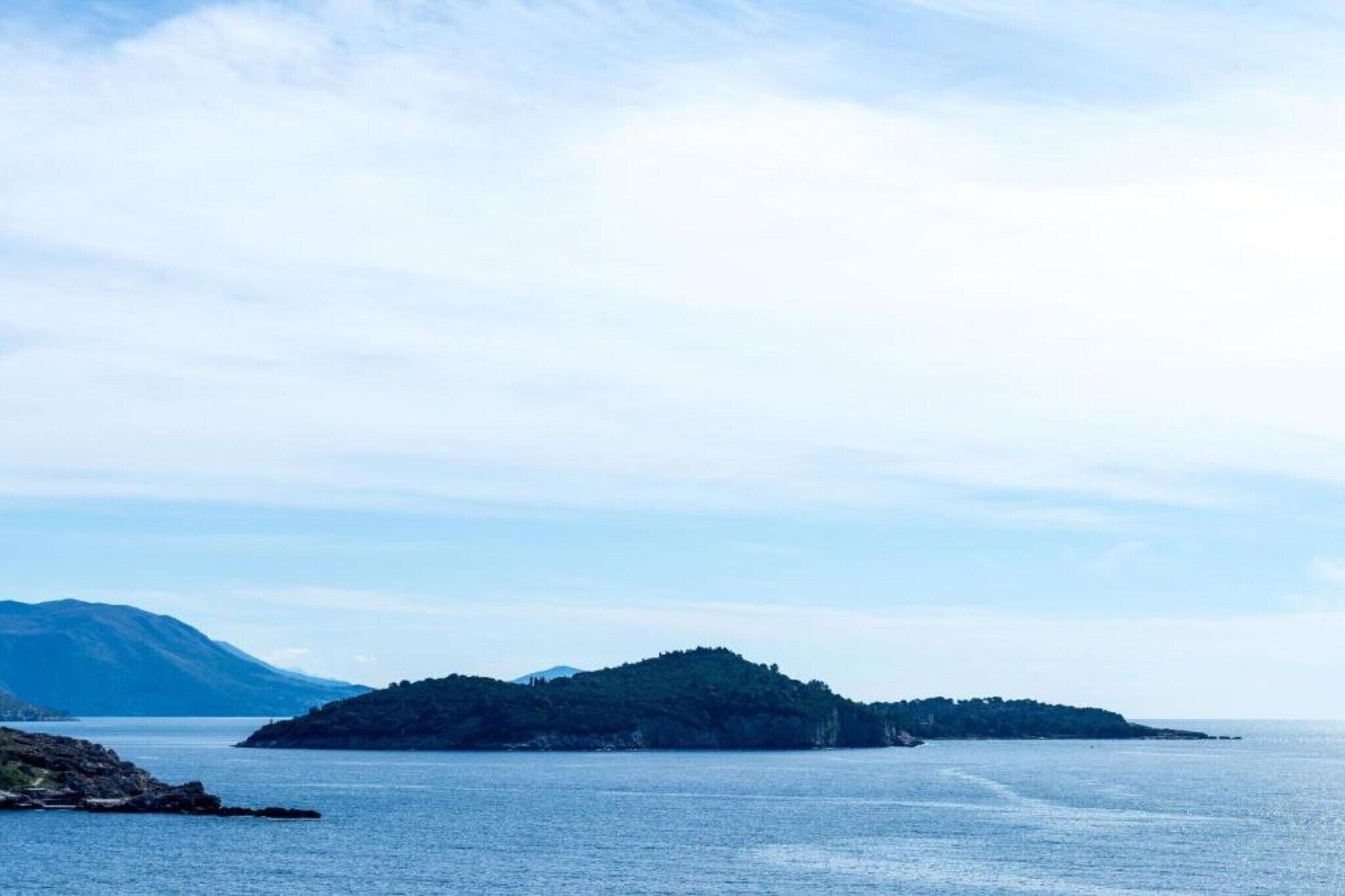 A coastal landscape with a small island and a mountain in the background.