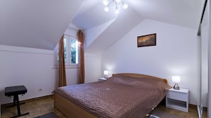 Un dormitorio con cama, mesitas de noche, un escritorio, una ventana con cortinas y una lámpara en el techo.