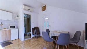 Cocina compacta con muebles blancos, microondas y un refrigerador pequeño. Cuenta con una zona de comedor con una mesa y cuatro sillas.