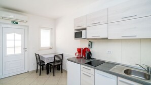 A modern kitchen with white cabinetry, a built-in microwave, a sink, and a dining area with a table and chairs.