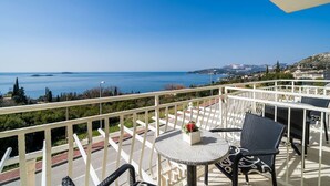 A balcony with a table and chairs, overlooking a coastal view.