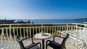 Un balcon avec une table ronde et deux chaises, offrant une vue panoramique sur la mer et les collines lointaines.