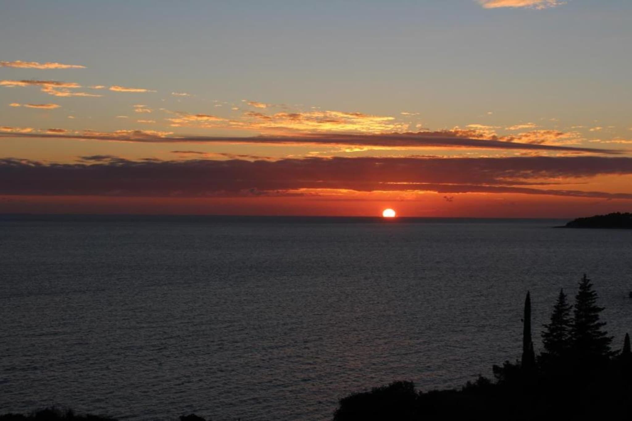 Un atardecer sobre un mar tranquilo con una masa de tierra a lo lejos.