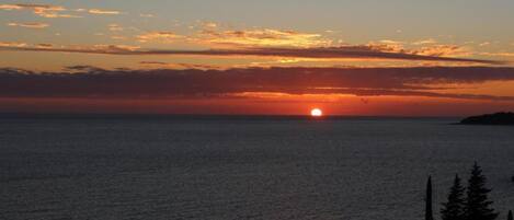 Un atardecer sobre un mar tranquilo con una masa de tierra a lo lejos.