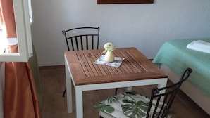 Pieni, siististi järjestetty huone, jossa on puinen pöytä ja kaksi tuolia, vihreä sänky ja ikkuna, jossa on verhot.