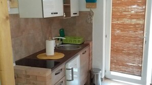 Pieni keittiö, jossa on pesuallas, vihreä kori ja roskakori.
