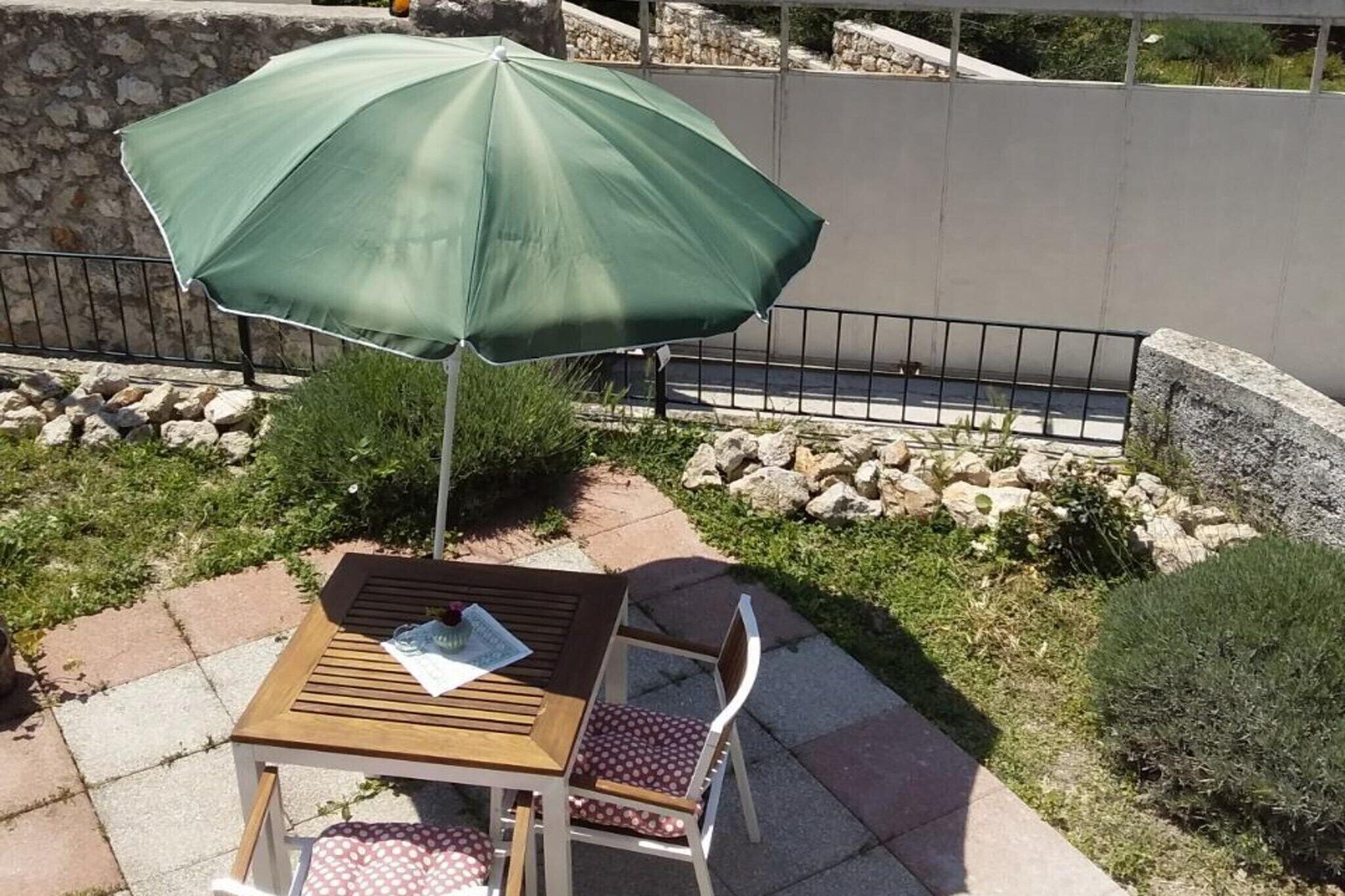 Une terrasse extérieure avec une table et une chaise en bois, un parasol vert et un mur de pierre en arrière-plan.
