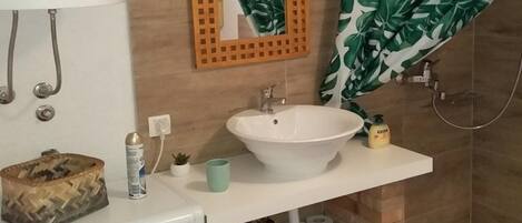 Een badkamer met een witte wastafel, een spiegel, een douche en een toilet.