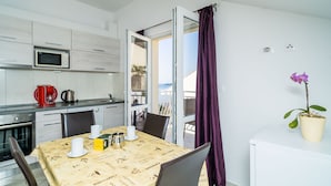 A compact kitchen with a microwave, coffee maker, and kettle. There's a dining table with chairs and a potted orchid. A sliding glass door leads to an outdoor balcony.