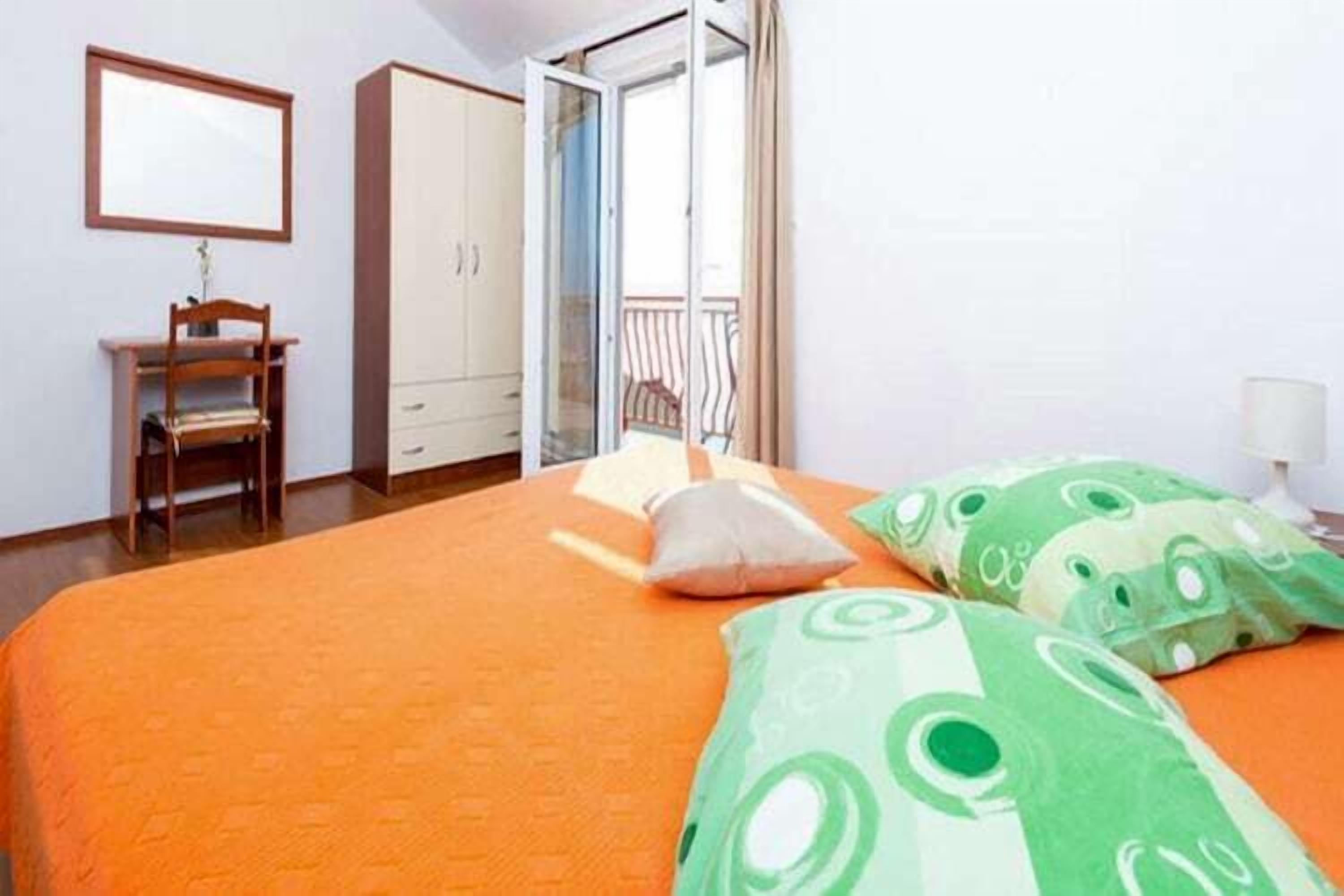 A bedroom with a bed, a desk, a wardrobe, and a sliding glass door leading to a balcony.