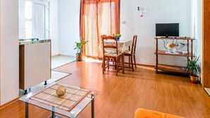 Ett kompakt bostadsutrymme med ett litet kök, en matplats och en tv som står på ett träställ.
