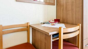 Un pequeño escritorio de madera con una silla, un espejo y una taza roja sobre la mesa.