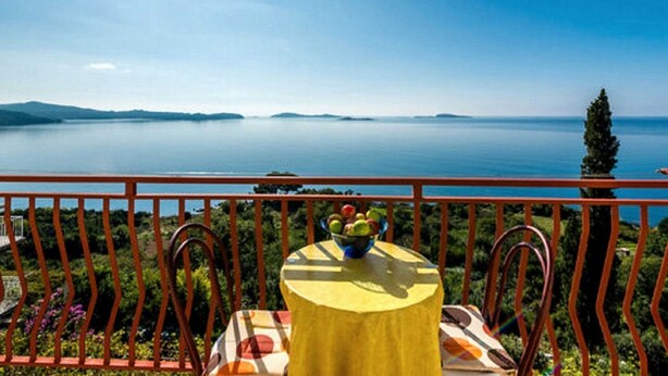 Ein Balkon mit Tisch und Stühlen, mit Blick auf ruhiges Wasser und ferne Berge.