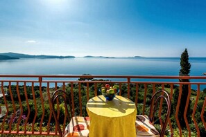 Un balcon avec une table et des chaises, donnant sur une étendue d’eau calme et des montagnes lointaines.