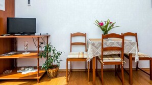 Ein kleiner Raum mit einem Holztisch, einem Fernseher, einem Tisch mit Stühlen und einer Topfpflanze.