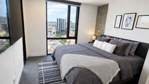 A modern bedroom with a large bed, a view of the city, and a mounted TV. - Distrito Revolution Suites  (Tijuana)