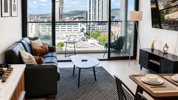 A modern living room with a sofa, coffee table, dining table, and a large window with a city view. - Distrito Revolution Suites  (Tijuana)