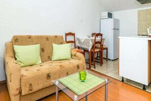Una habitación pequeña y amoblada con sofá, mesa de comedor, sillas, zona de cocina con refrigerador y microondas.