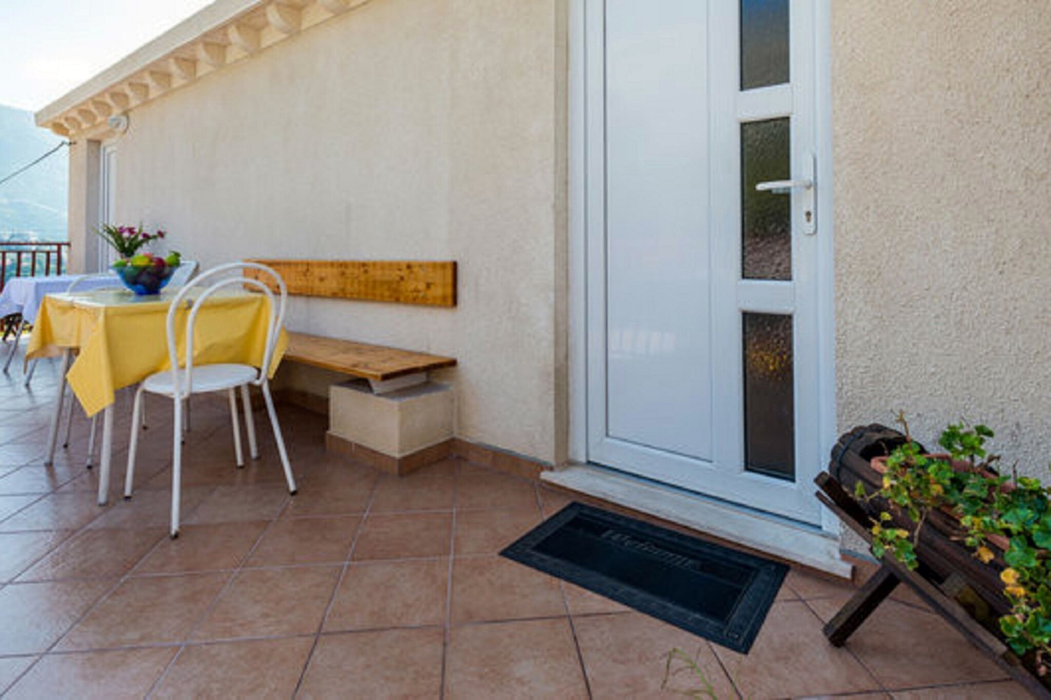 Un patio con tavolo e sedie, una panca e una porta con un pannello in vetro.